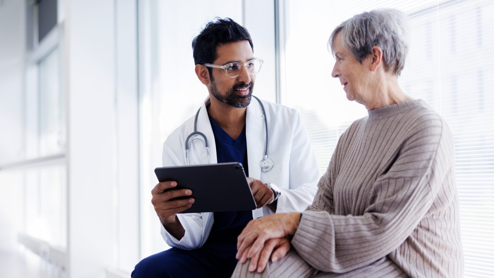Doctor Reviews Information on Tablet with Older Patient