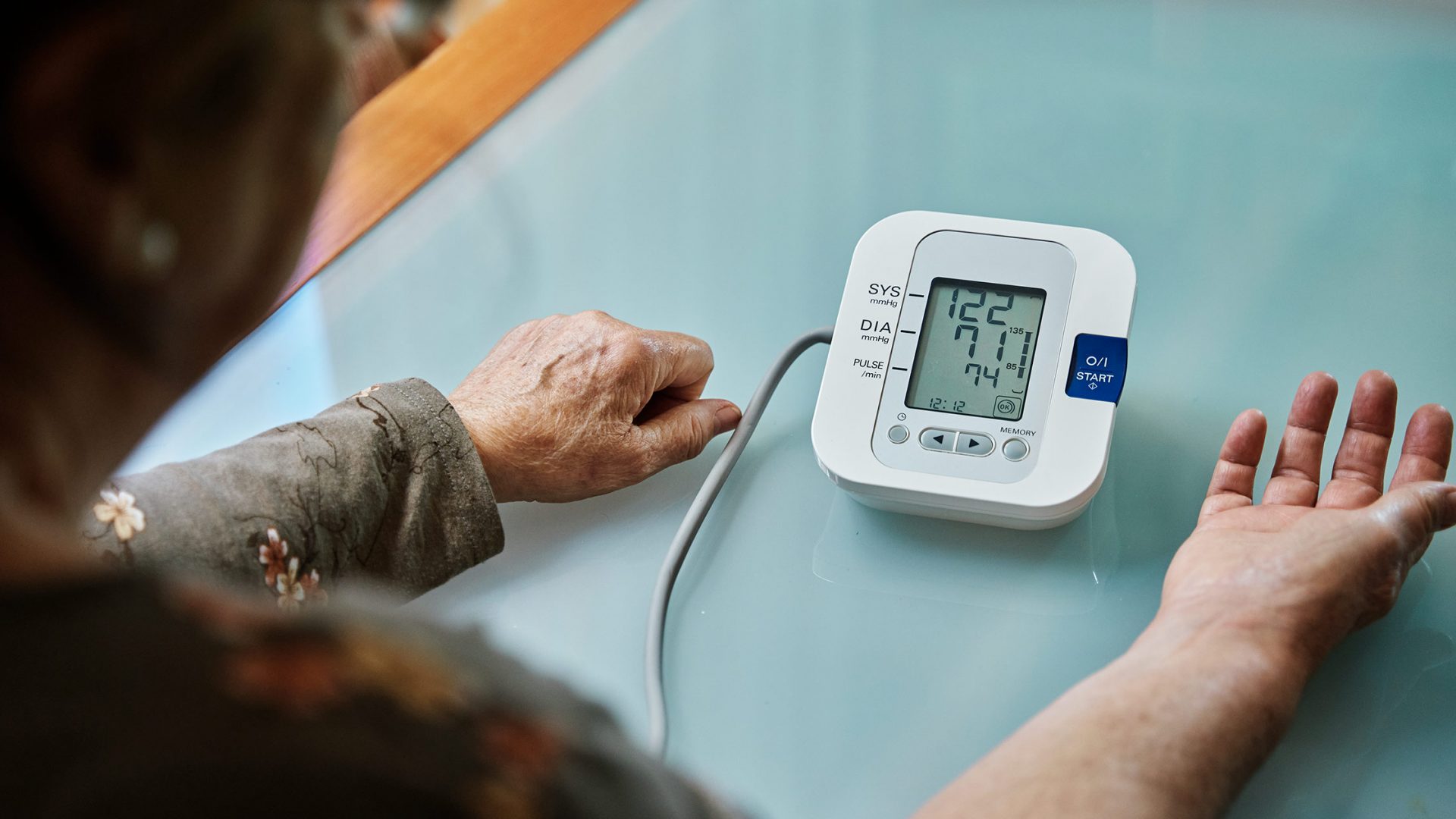 Older Adult Sitting at Table and Looking at Blood Pressure Monitor Results