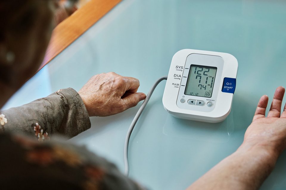 Older Adult Sitting at Table and Looking at Blood Pressure Monitor Results