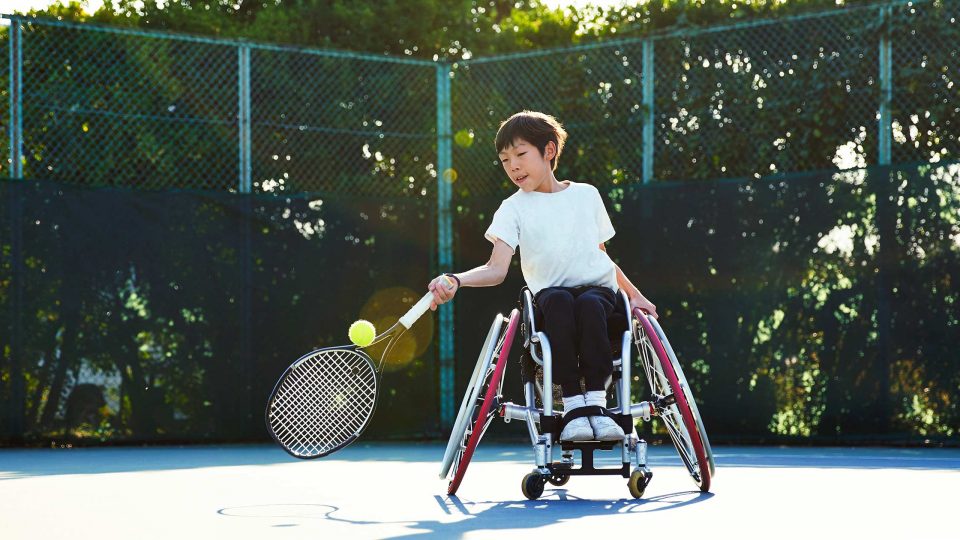 Young child in wheelchair playing tennis on a tennis court