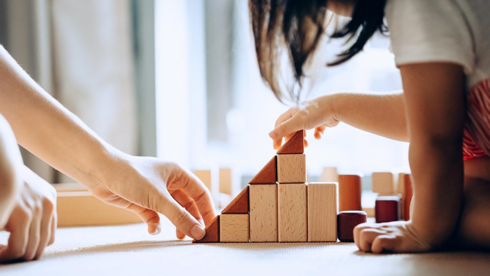 Close up view of parent and child sitting on the floor playing with wooden building blocks together
