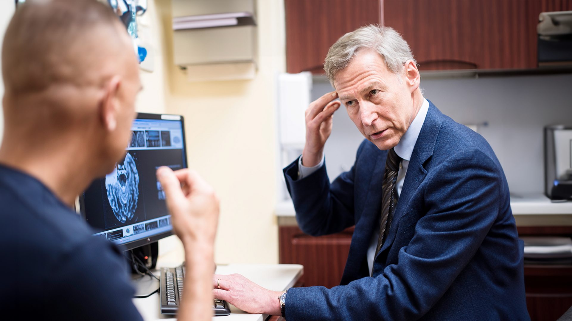 Dr. Orrin Devinsky pointing at the side of his head while reviewing brain imaging results on a computer with a patient