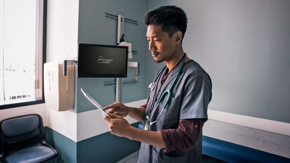 Healthcare provider wearing scrubs and stethoscope working on digital tablet in hospital