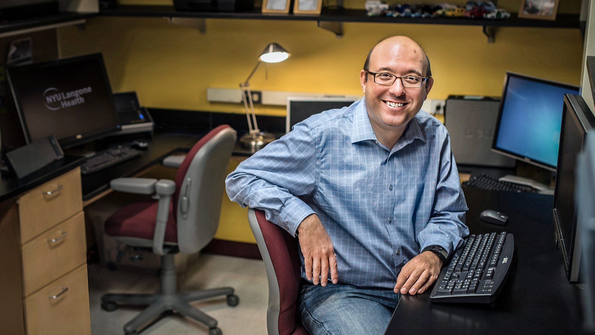 Dr. David M. Landsberger seated a computer desk and smiling