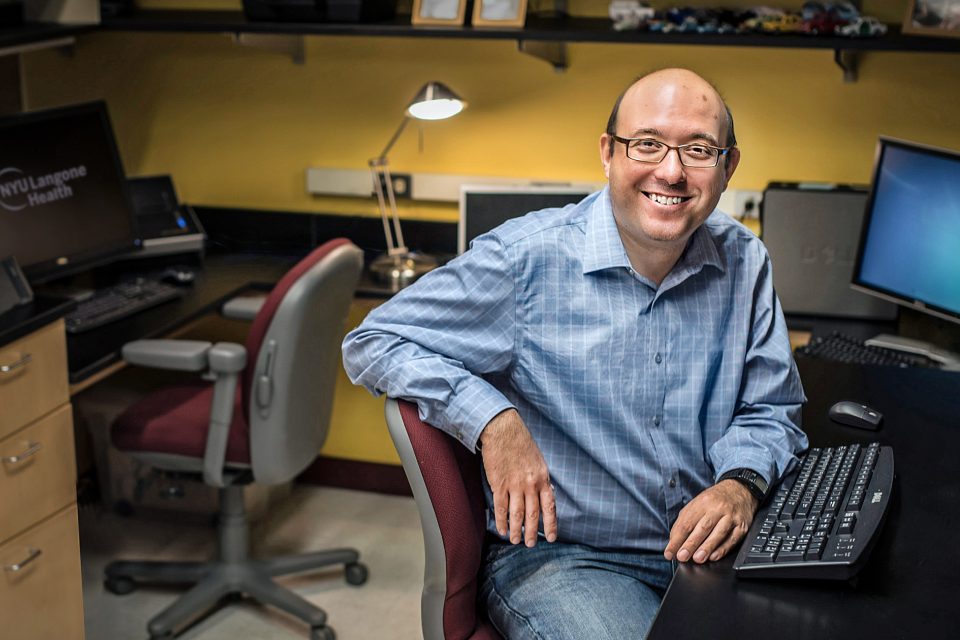 Dr. David M. Landsberger seated a computer desk and smiling