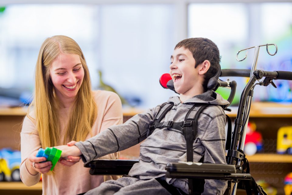 Smiling child in wheelchair playing with blocks with assistance from a caregiver