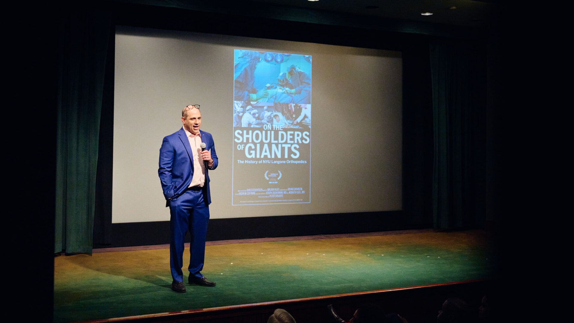 Dr. Egol stands in front of a movie screen showing a poster of the movie.