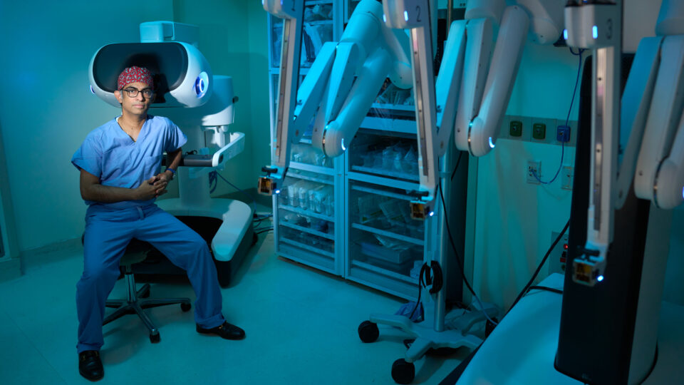 Umamaheswar Duvvuri, MD, PhD sitting in a chair near the da Vinci 5 robotic surgical system.