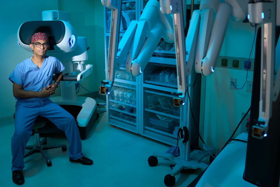 Umamaheswar Duvvuri, MD, PhD sitting in a chair near the da Vinci 5 robotic surgical system.